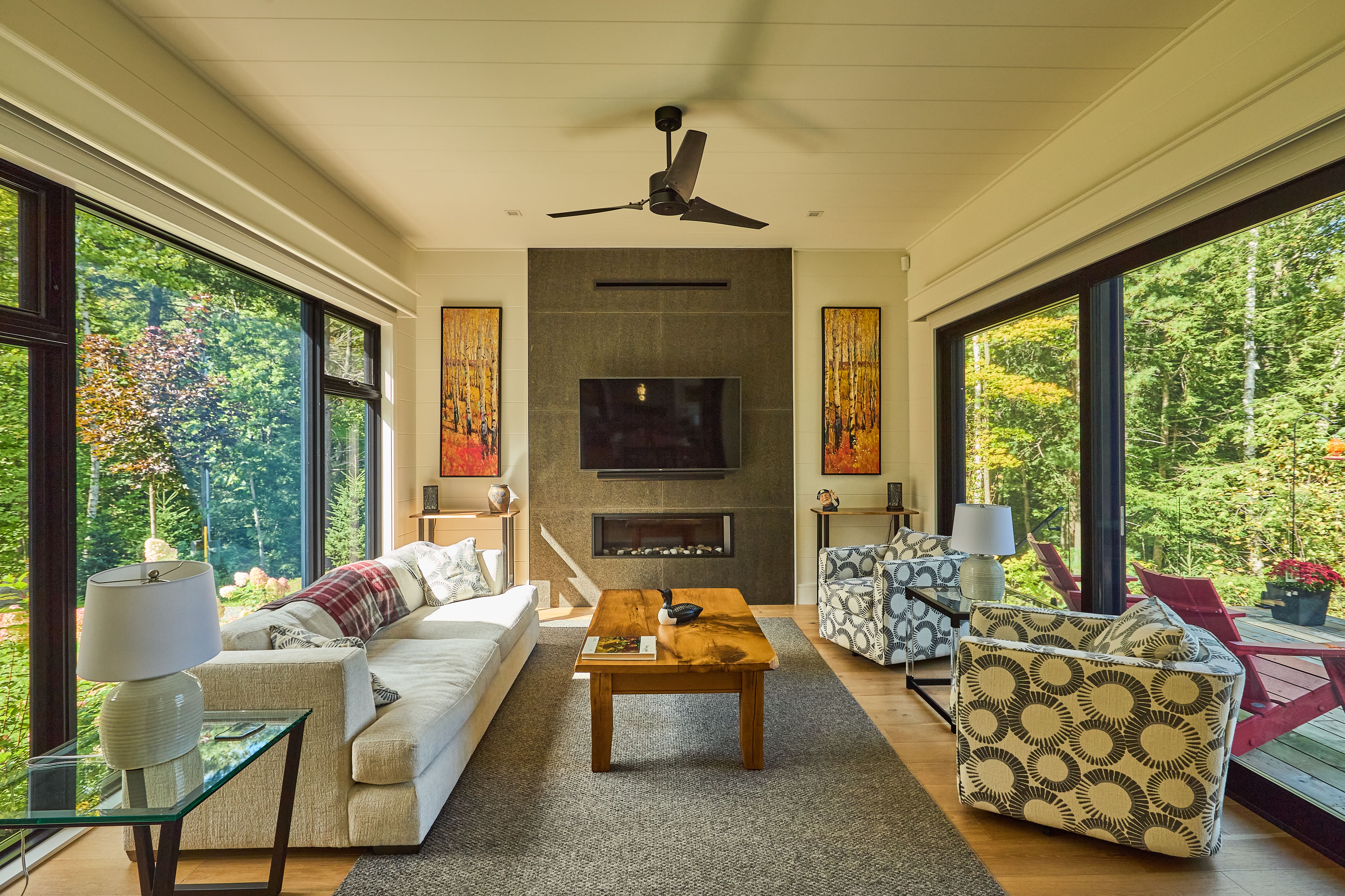 Cozy living room with views of forest on either side through large, black-framed windows.