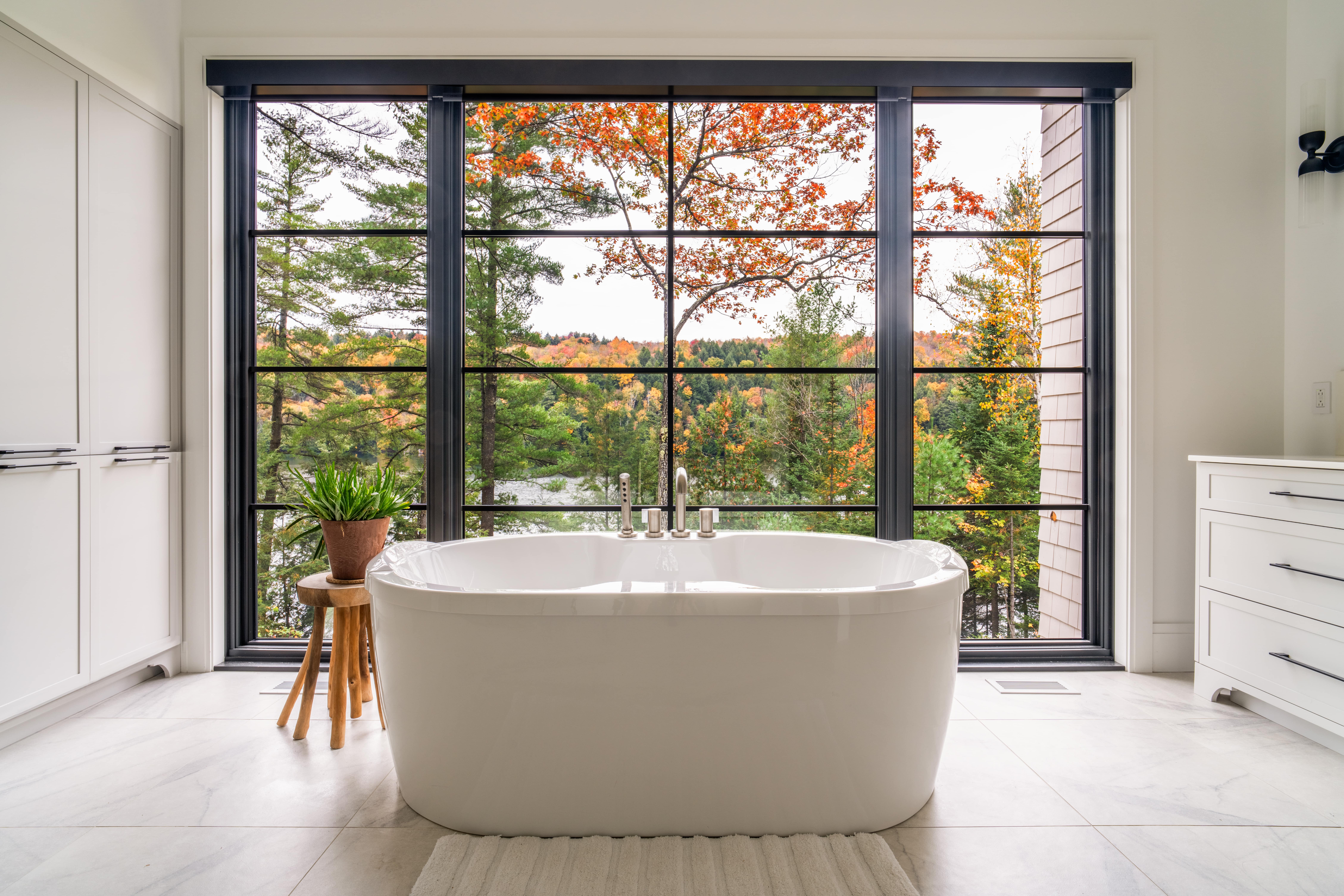 Elegant bathroom featuring a bathtub centered on large black-framed windows overlooking a lake.