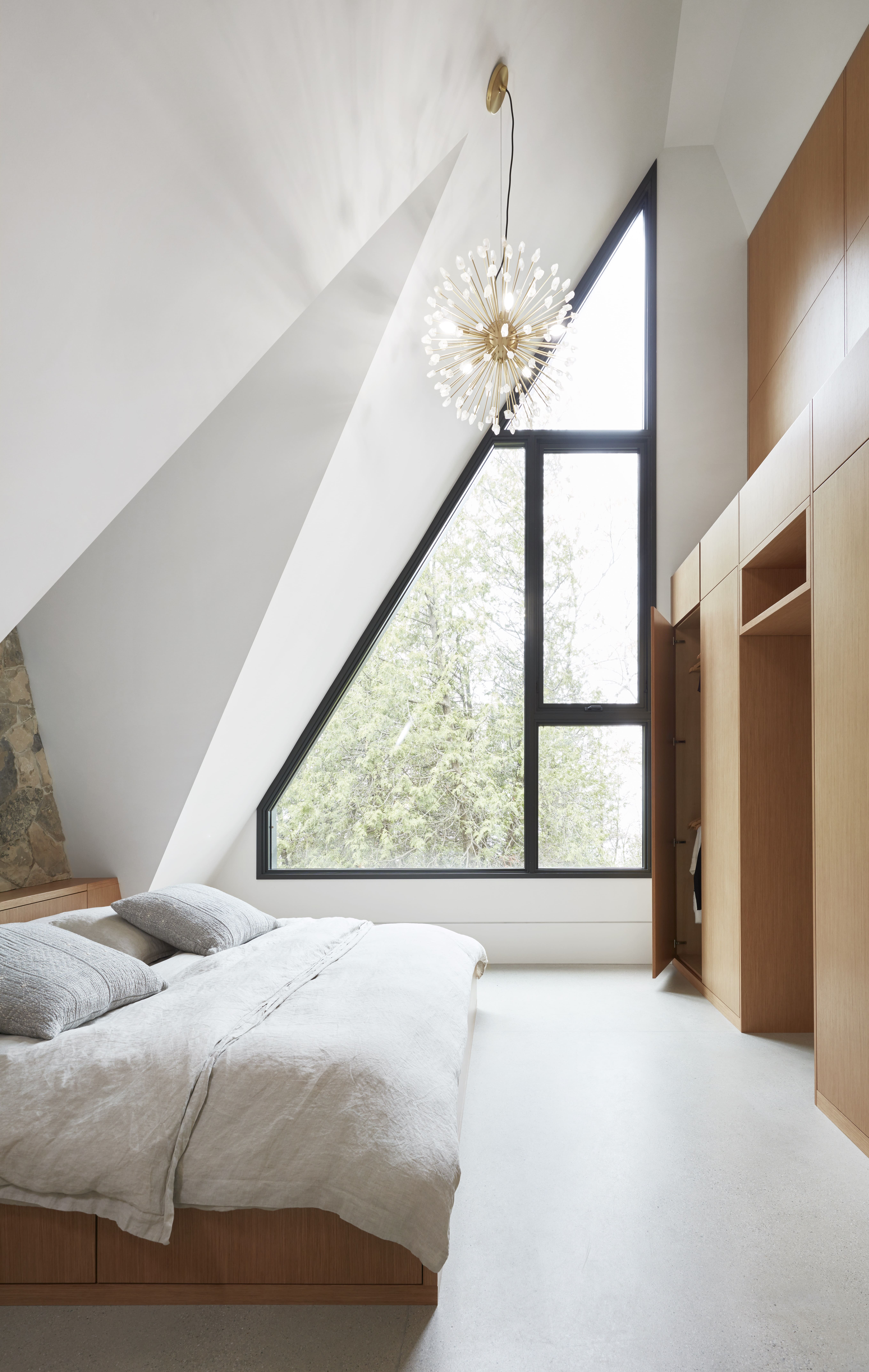 Modern bedroom with dramatic ceiling slope and right triangle shaped window.