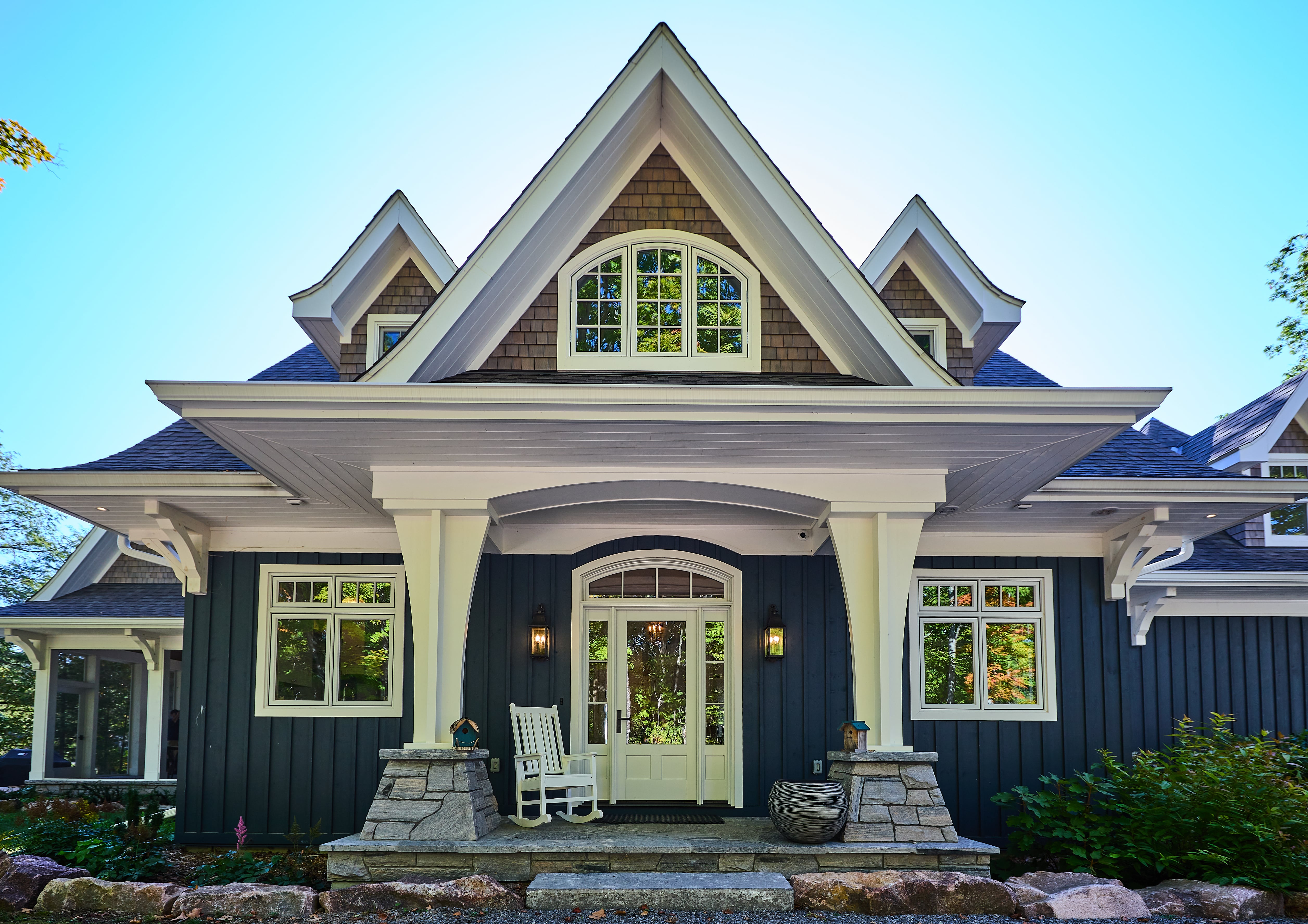Exterior of craftsman-style home with dramatic roofline and arched white windows and doors.