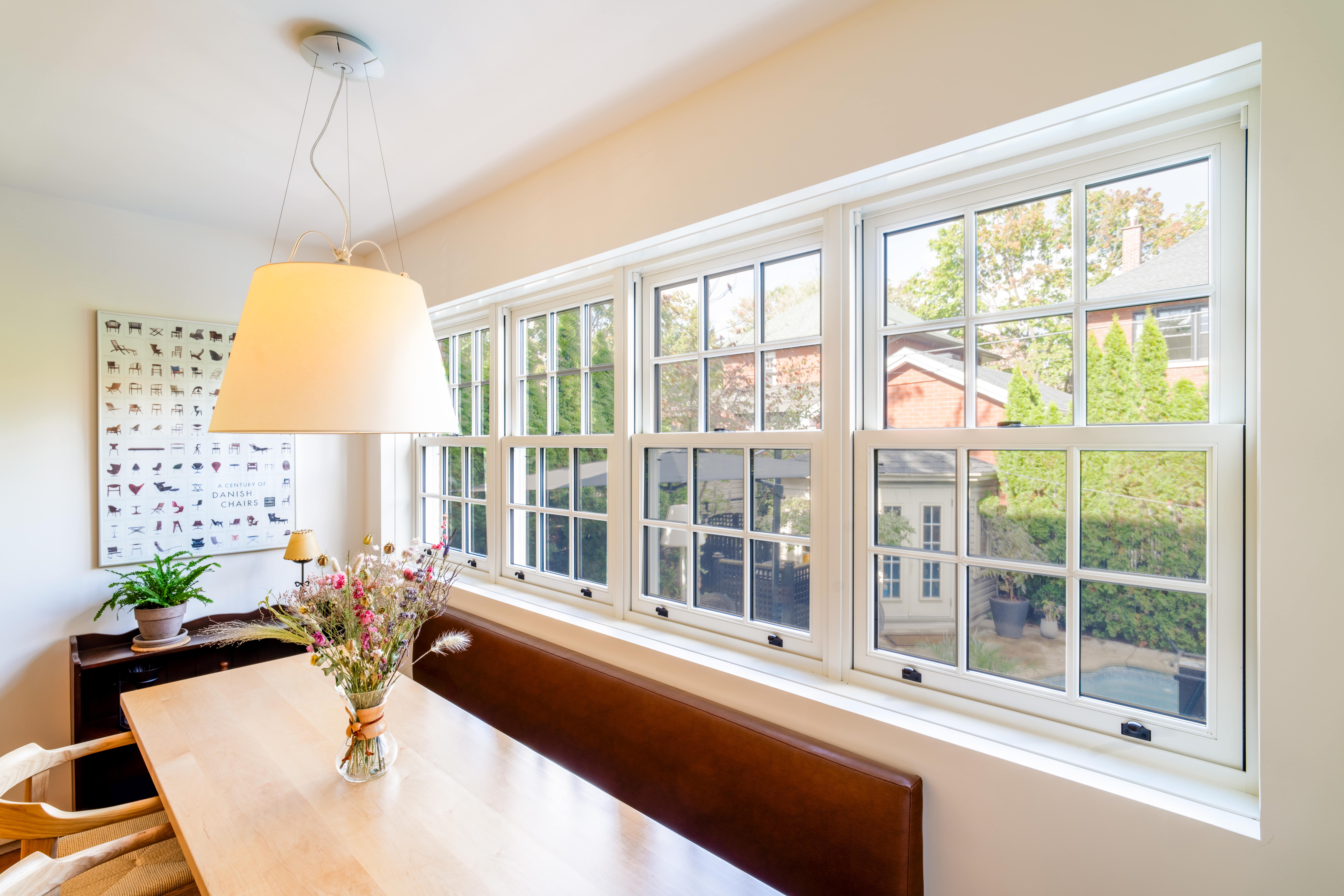 Bright dining nook with a wooden table, large pendant light, and wide windows overlooking a backyard.