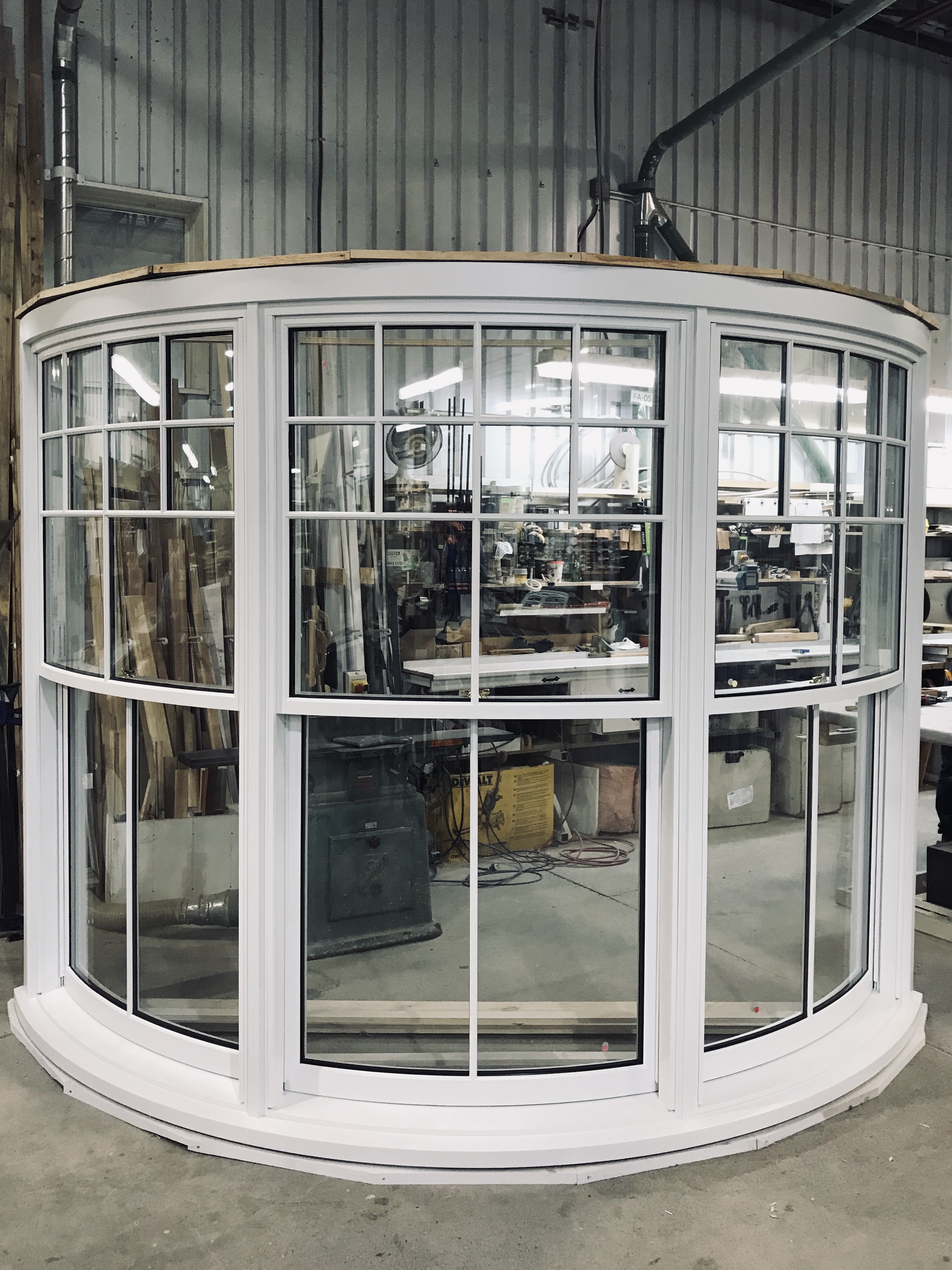 Curved white bay window with multiple panes, displayed in a workshop with tools and equipment in the background.