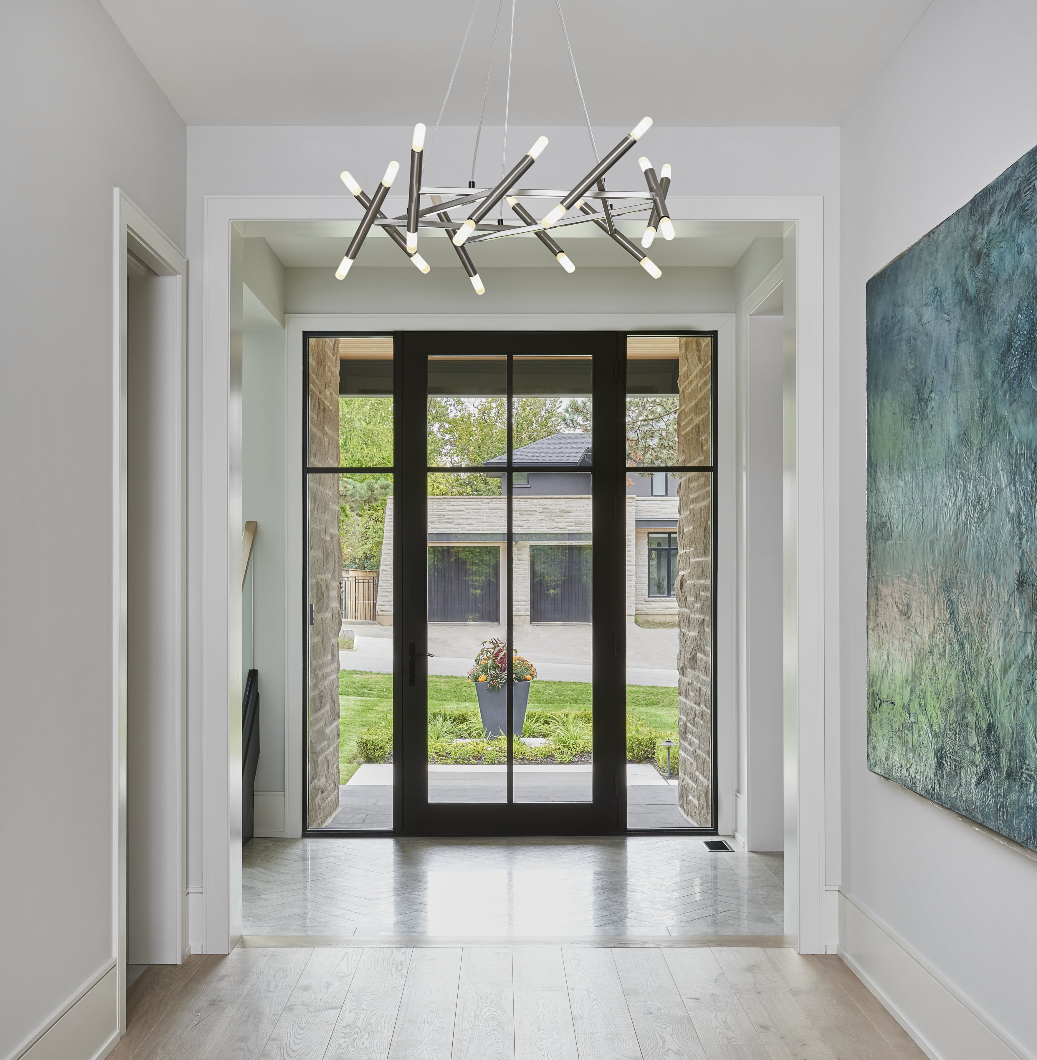 Airy entryway with an abstract chandelier, double glass doors, and a green-blue painting on the wall.