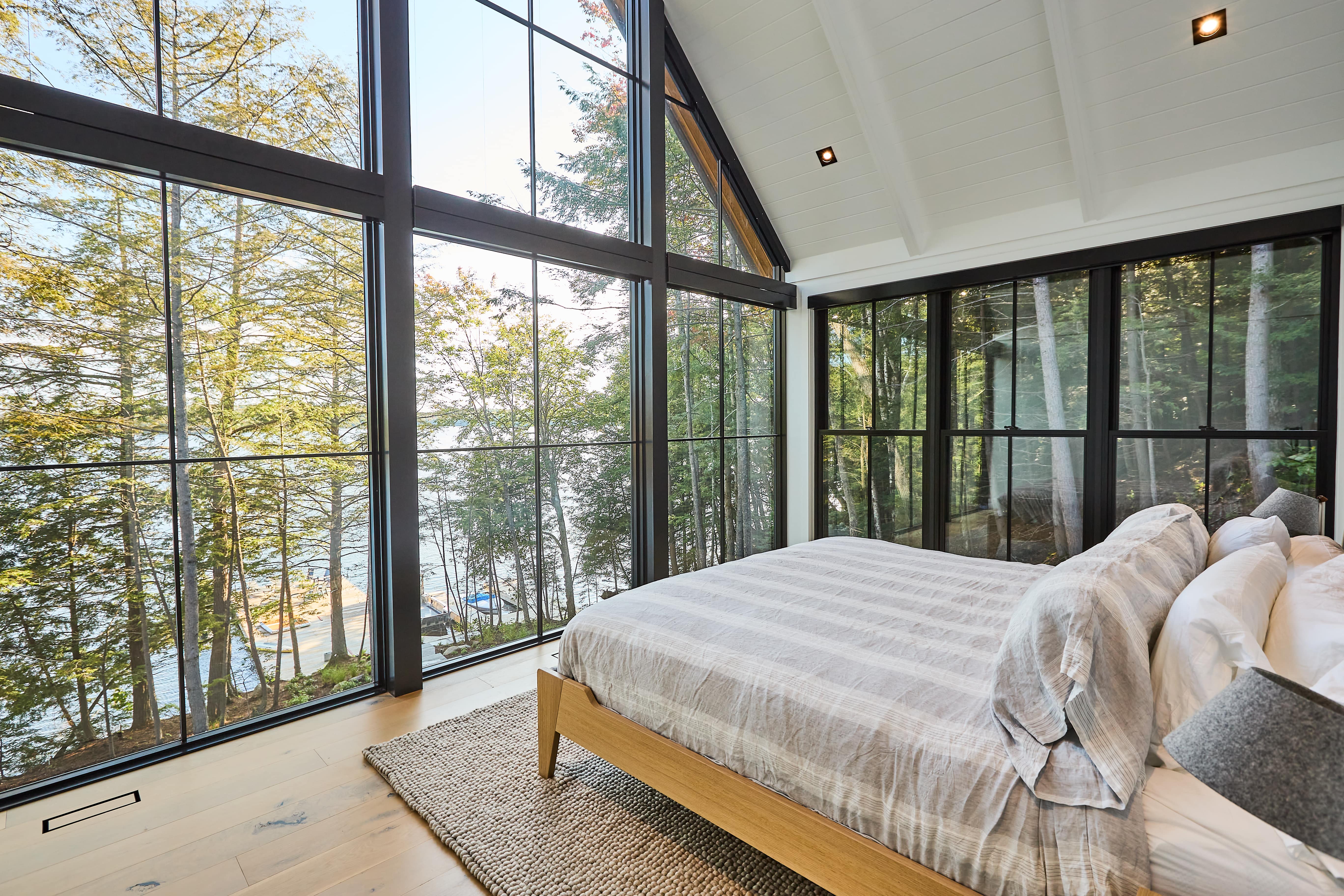 Modern bedroom with floor-to-celing windows following the slope of vaulted ceiling and overlooking a lake.